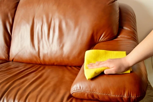 Person cleaning a leather sofa with a yellow cloth.