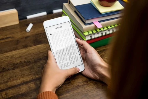 Close-up of a phone displaying an e-book, with notebooks in the background.