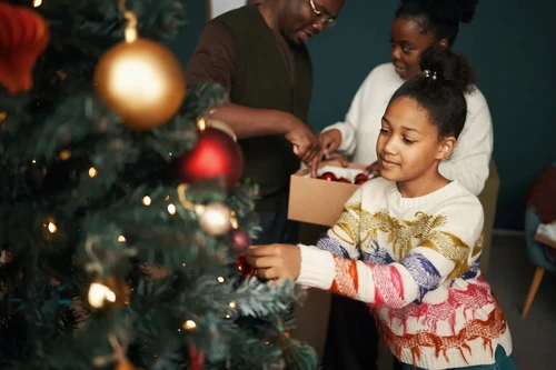 Family packing holiday decorations into labeled storage boxes beside a Christmas tree in a living room.