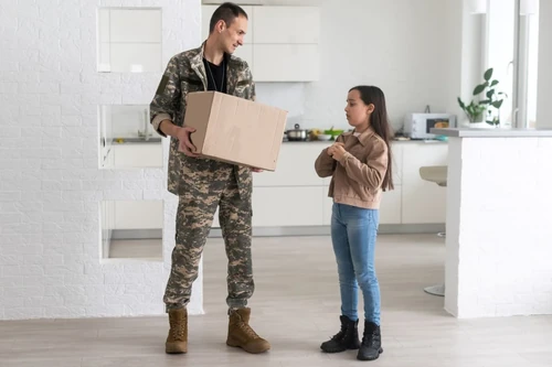 Military parent holding a cardboard box, preparing to move, while daughter stands nearby.